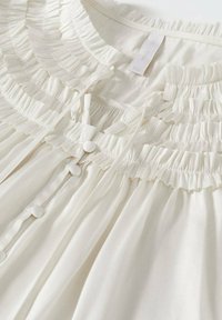 Lichte crème blouse met ruffle-details langs de halslijn en voorkant, voorzien van met stof bedekte knopen en een gladde textuur.