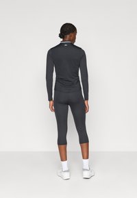 Top de manga larga gris oscuro y leggings cortos, ambos hechos de un material suave y elástico. Presenta un logo discreto en el cuello. Calzado blanco.