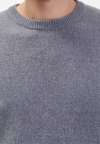 Grau gestrickter Pullover mit strukturierten Oberflächen und einem gerippten Rundhalsausschnitt. Der Stoff wirkt weich und mitteldick.