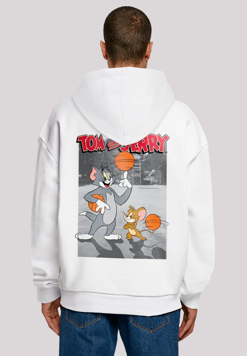 Bílá mikina s kapucí, která má grafický potisk s Tomem a Jerrym, jak hrají basketbal. Design obsahuje jasné barvy a výrazný text nahoře.