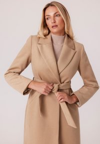 Beżowy płaszcz z paskiem, wykonany z teksturowanej mieszanki wełny, z kołnierzem z wyłogami, długimi rękawami i kieszeniami bocznymi.