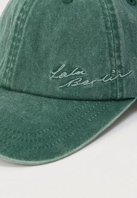 Πράσινο καπέλο από τζιν με καμπυλωτή γείσα, με λευκό κεντημένο λογότυπο "Lala Berlin" στο εμπρόσθιο μέρος. Υφάσμα με υφή και ραμμένες λεπτομέρειες.