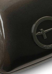 Glänzende braune Hartschalen-Tasche mit einem kreisförmigen schwarzen Logo mit vereinfachtem Design auf der Vorderseite; glatte Textur, leichter Glanz.