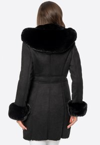 Czarny płaszcz zamszowy z dużym, miękkim kołnierzem z czarnego futra i futrzanymi mankietami. Dopasowany fason z paskiem w talii, z pionowymi szwami.