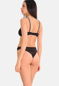 Ensemble de lingerie noire comprenant un soutien-gorge balconnet avec des fines bretelles et un string assorti. Le tissu a une texture transparente avec des accents en dentelle.