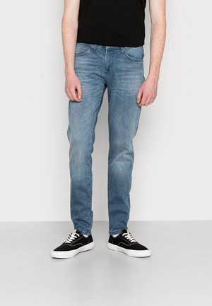 Vervaagde lichtblauwe spijkerbroek met een rechte pasvorm, vijf zakken en subtiele whisker-effecten, gecombineerd met zwarte low-top sneakers.