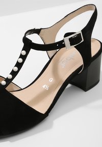 Sandale femme en daim noir avec talon bloc, bride de cheville avec boucle argentée et perles blanches décoratives sur la bride avant.