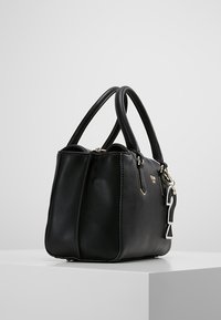 Zwarte lederen handtas met twee afgeronde handvatten, een gladde textuur en een hanger in de vorm van een vraagteken. Heeft goudkleurige metalen accenten.