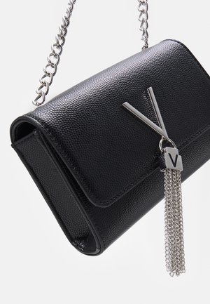 Sac en cuir noir texturé avec une bandoulière en chaîne argentée et un fermoir en "V" argenté, ornée d'un gland composé de plusieurs chaînes argentées.