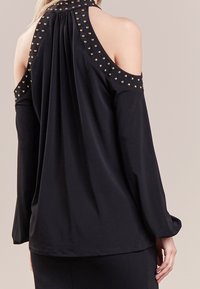 Czarny longsleeve z dekoltem typu cold shoulder, plisowany z tyłu, z dekoracyjnymi złotymi ćwiekami na ramionach, wykonany z gładkiego materiału.