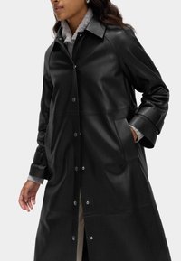 Černý kožený trenčkot s límečkem, zapínáním na patentky, bočními kapsami a šedým fleece podšívkou na manžetách pro větší pohodlí.