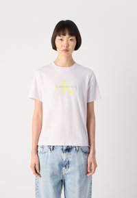 Lys lilla bomull t-skjorte med korte ermer. Har et sentralt logo "Calvin Klein" i grønn og gul skrift. Avslappet passform.