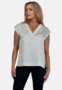 Bluzka z krótkim rękawem w kolorze białym z czarnym nakrapianym wzorem. Posiada dekolt w kształcie litery V i boczne rozcięcia, wykonana z gładkiego materiału.