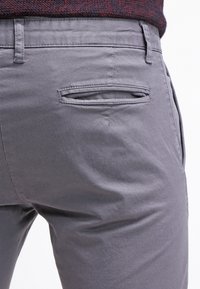 Šedé kalhoty vyrobené z hladké bavlněné tkaniny, s zadní kapsou s rozparkem a zesíleným švem pro zvýšení odolnosti.