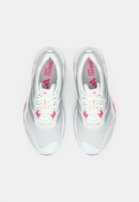 Scarpe sportive bianche con tomaia in mesh testurizzato, accenti rosa e grigi, lacci piatti e la scritta "Adidas Training" sulle solette.