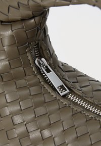 Woven olive-green leather bag featuring a silver zipper detail and a textured finish. The design is structured with a loop handle.