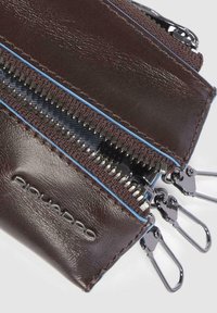 Brown leather wallet featuring two silver zippers, blue accents, and a textured surface. Marked with "Piquadro" logo.