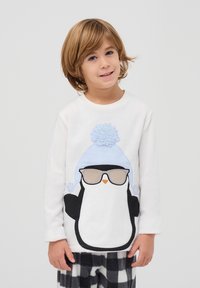 Biała polarowa bluza z rysunkowym pingwinem w jasnoniebieskiej czapce i okularach, w połączeniu z czarno-białymi spodniami w kratkę.