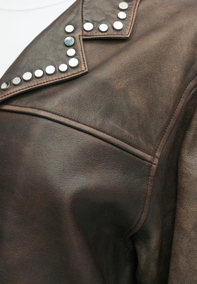 Braune Lederjacke mit strukturiertem Oberflächenmaterial, ausgestattet mit silbernen Nieten am Kragen. Enthält detaillierte Nähte und ein strukturiertes Design.