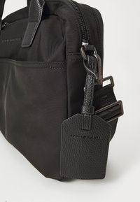 Zwarte nylon schoudertas met getextureerde leren accenten, ritssluiting, verstelbare schouderriem en een bagagetag met geperst logo detail.