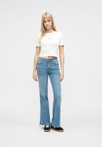 Lichtgekleurde, geribbelde crop top met een klein rood hartje, gecombineerd met lichtblauwe, high-waisted flare jeans en zwarte plateau schoenen.