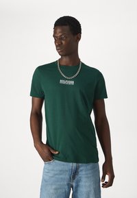T-shirt verde in cotone con maniche corte, caratterizzato da una stampa del logo bianco sul petto e una collana in argento per un tocco di dettaglio.