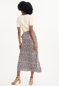 Top corto a righe color crema abbinato a una gonna avvolgente a motivi blu navy e beige, con vita legata e un orlo fluido.
