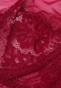 Bourgondisch kanten stof met bloempatronen en een gestructureerd oppervlak, gelaagd over een glad, doorschijnend roze basismateriaal.