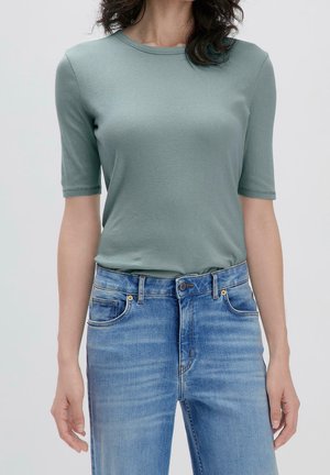 Krótki rękaw, top z okrągłym dekoltem wykonany z miękkiego, jasnooliwkowego materiału, zestawiony z jasnoniebieskimi dżinsami o klasycznym kroju z delikatnym efektem sprania.
