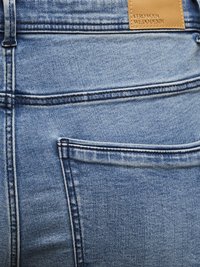 Jasnoniebieskie dżinsy z tylną kieszenią ozdobioną kontrastującymi przeszyciami oraz skórzaną metką. Faktura jest gładka z lekkim wyblaknięciem.