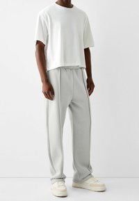 White short-sleeve t-shirt paired with light gray sweatpants featuring elastic waistband and side stripes, worn with beige sneakers.