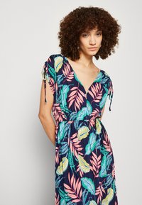 Abito lungo con profonda scollatura a V, maniche corte, motivi fogliari floreali in verde, rosa e giallo su uno sfondo blu navy, e vita elastica.