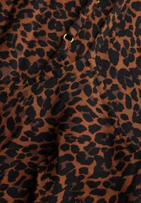Leopardprint stof med en brun baggrund og sorte pletter. Glat tekstur med en subtil glans. Har et guldaccent detalje.