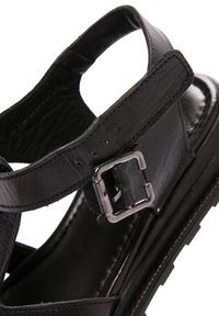 Sandal in pelle nera con fibbia regolabile, design aperto sulla punta e superficie texturizzata. Suola robusta con cuciture visibili.