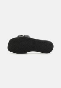Suola di scarpa nera con una superficie in gomma testurizzata, caratterizzata da un design del battistrada a forma di cuore e una forma arrotondata. Nessun hardware visibile.