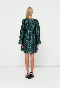 Green floral dress with long, puffed sleeves, gathered waist, and a short hem. Fabric features a glossy finish and intricate leaf patterns.
