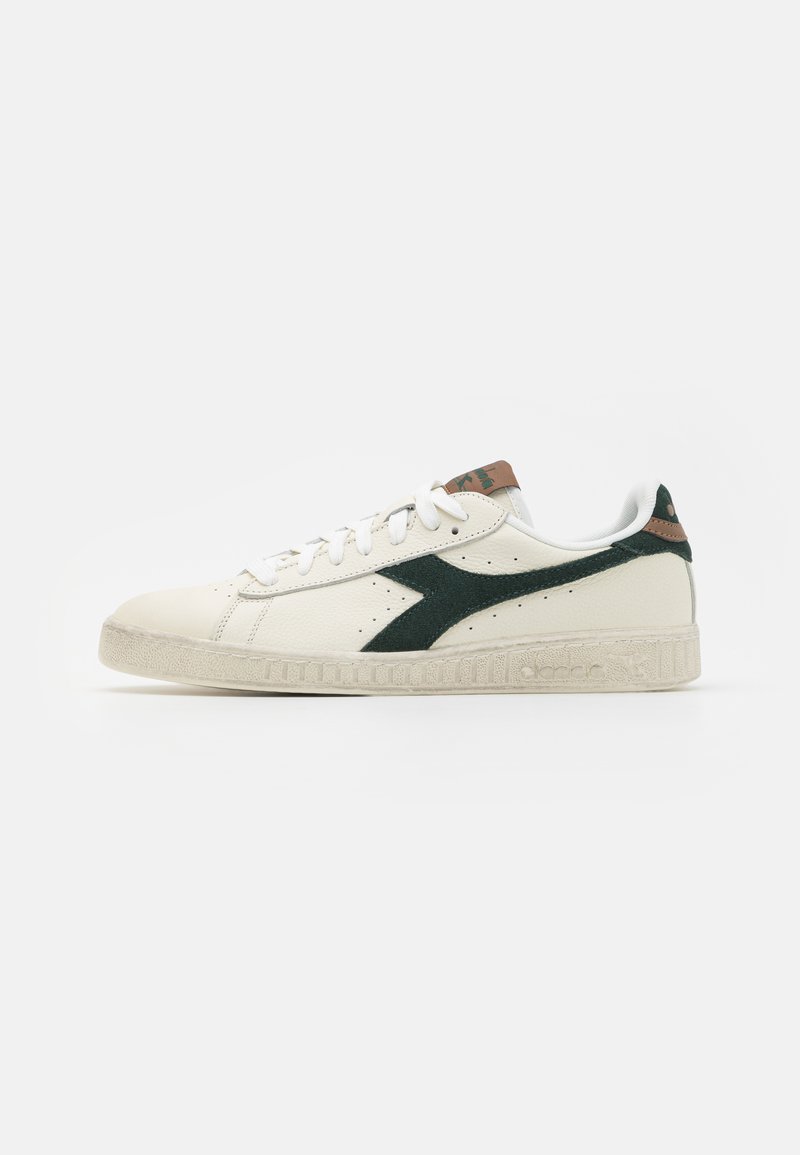 Hvit lær sneaker med grønn semsket akcent, teksturert gummisåle og brun hældetalj. Snøring med perforeringer på siden.