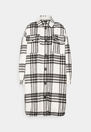 Pitkä mustavalkoinen ruudullinen painonappitakki, jossa on kaksi rintataskua läpällä ja terävä kaulus, esillä yksivärisellä vaalealla taustalla.