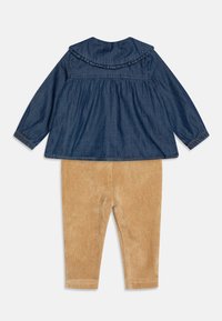 Denim top with ruffled collar and long sleeves, paired with beige corduroy pants. Top features gathered bodice and elastic cuffs.