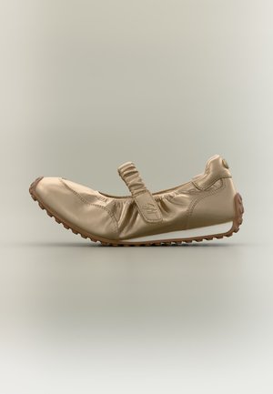 Chaussure décontractée beige en cuir souple avec sangle élastique, semelle en caoutchouc et bande de roulement texturée pour une bonne adhérence, montrée de profil sur un fond uni.