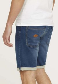Shorts en denim bleu foncé avec des ourlets retroussés. Présente une étiquette en cuir texturé beige sur la poche arrière et des détails de couture standards.