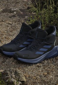 Botas de senderismo negras y azules con un upper texturizado, que cuentan con la marca Gore-Tex, diseño de cordones y una suela robusta adecuada para terrenos al aire libre.