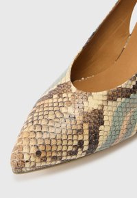Bézs, barna és zöldes-kék árnyalatú, texturált kígyómintás anyagból készült hegyes orrú cipő. Nyitott oldalakkal rendelkezik.