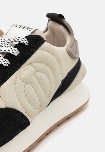 Zapatillas con un upper de textil beige y acentos en ante negro, cordones blancos y un logotipo pronunciado. Suela blanca gruesa con una suela de goma.