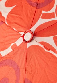 Κόκκινο και λευκό ύφασμα με φλοράλ σχέδιο, με ένα κεντρικό λευκό κουμπί με ραβδώσεις περιβαλλόμενο από ένα ύφασμα σε σχήμα ροζέτας. Υφή επιφάνειας.