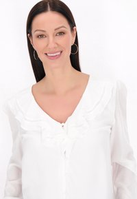 Blusa bianca con scollo arricciato e chiusura a bottoni, con maniche lunghe trasparenti e una texture leggera, arricchita da un design sottile.