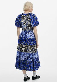 Maxi mekko, jossa on puffi-hihat, sekoitus kukka- ja abstrakteja kuvioita sinisen ja mustan sävyissä, sekä kerroksellinen hameen design.