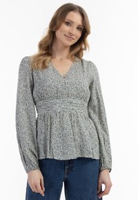 Bluse mit floralem Muster, V-Ausschnitt, geraffter Taille und langen Puffärmeln. Hergestellt aus weichem Stoff in hellen Tönen von Blau, Gelb und Grün.