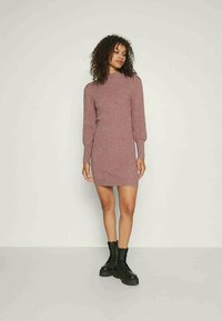 Vestido de malha canelada em rosa antigo com gola alta, mangas bufantes longas e silhueta ajustada, combinado com botas de combate pretas com atacadores.