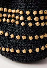 Juodas nertų audinys iš arti, papuoštas keliais eilėmis šviesių medinių kubo formos karoliukų, tolygiai susiūtais horizontaliomis linijomis.